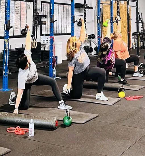 Women performing stretching and mobility exercises with kettlebells during group class at Freedom Fitness gym in St. Peters, Missouri